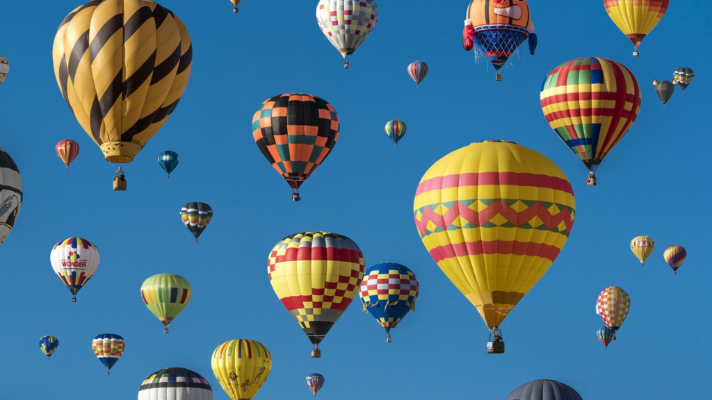 Many colorful hot air baloons flying, with a background of blue sky. 