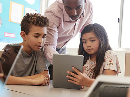 Teacher among school kids using tablet in class